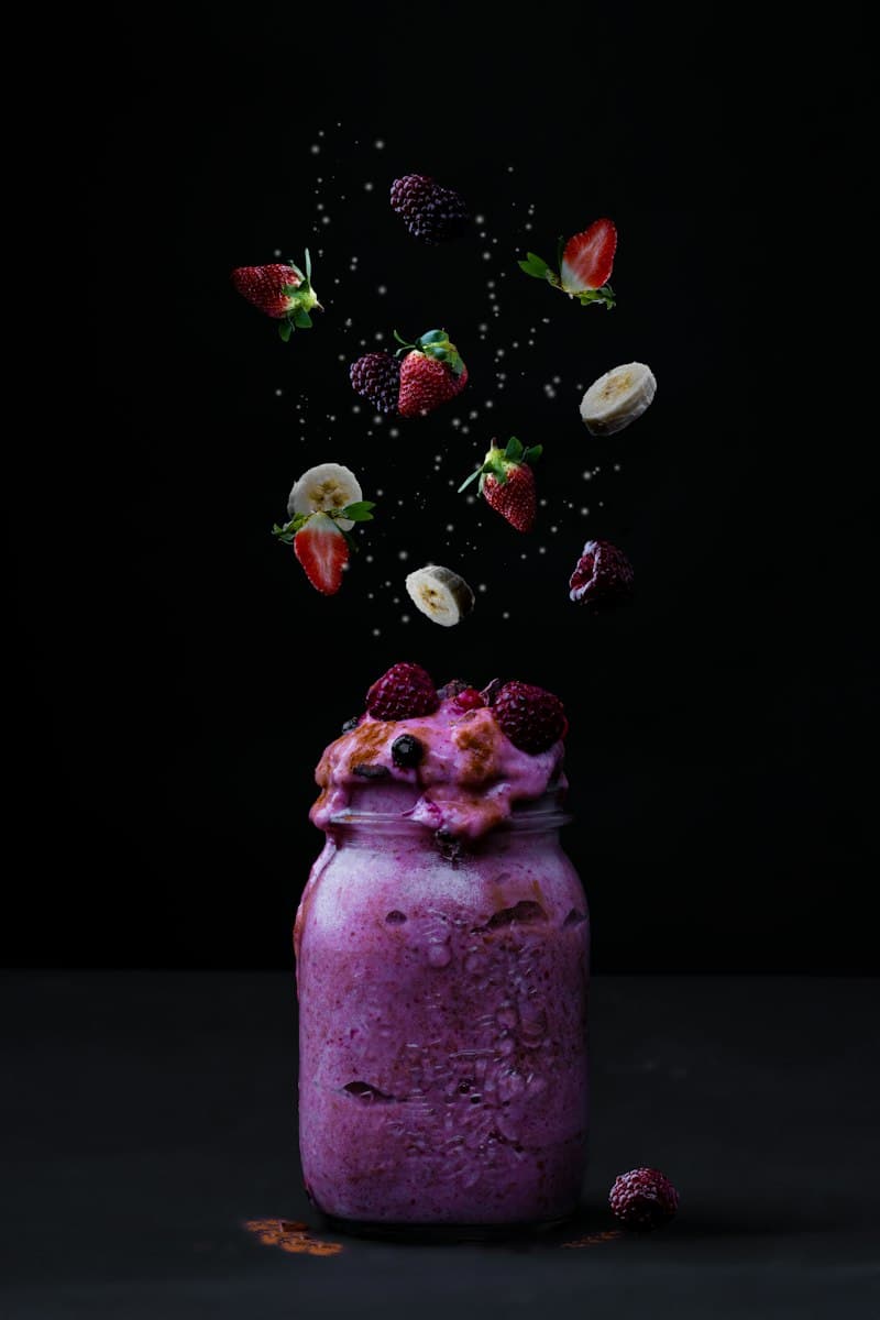 A purple smoothie in a jar with berries falling above it