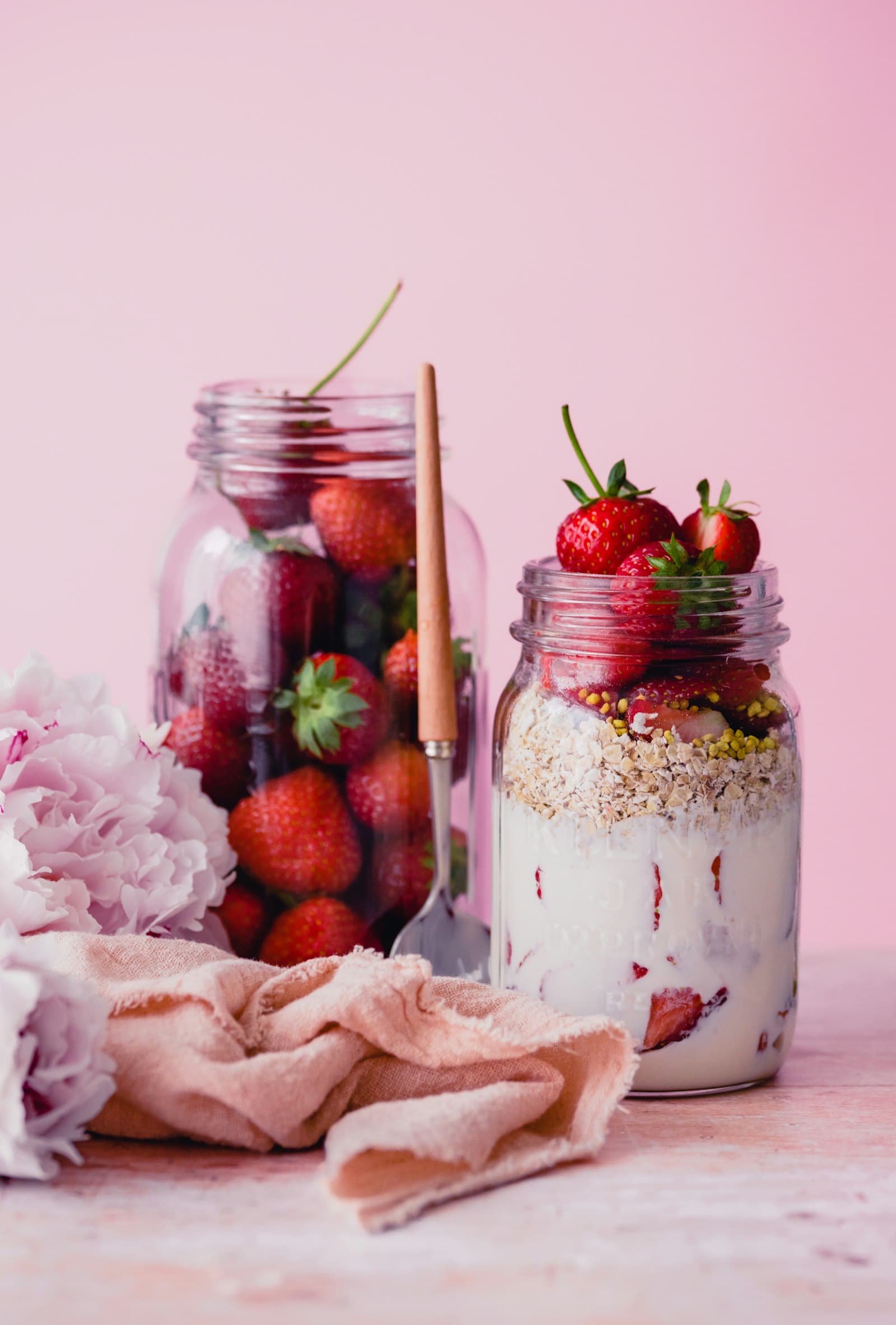 Glass jars of fresh strawberries and a granola parfait on a blush pink table