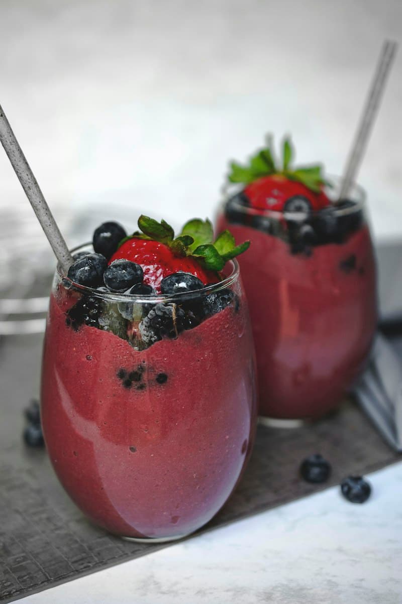 Two glasses of deep red berry smoothie topped with blueberries and a strawberry