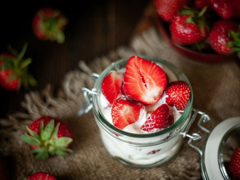 A glass jar of cream topped with halved fresh strawberries