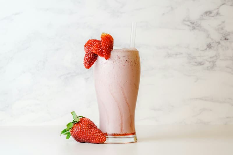 A pale pink smoothie in a tall glass garnished with a strawberry