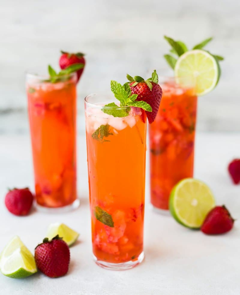 Three tall glasses of red strawberry drink with mint, lime and whole strawberries