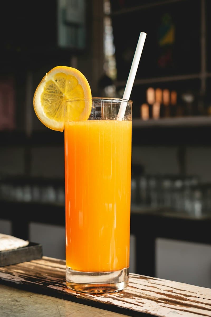 A glass of bright orange juice with a straw and a citrus slice on the rim