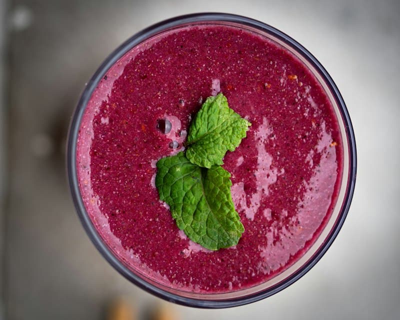 A purple berry smoothie seen from above, topped with a mint sprig