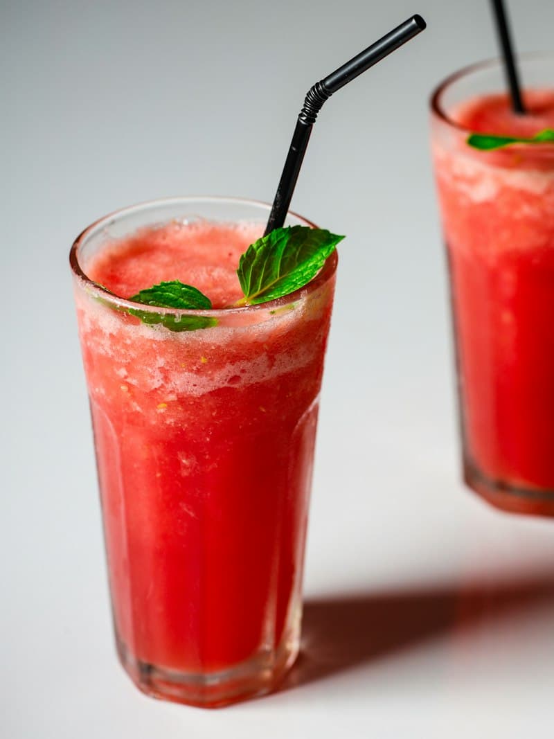 Two glasses of red watermelon juice with mint leaves and black straws